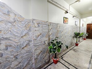Un couloir aux murs de marbre, agrémenté de plantes en pot et de tableaux encadrés.