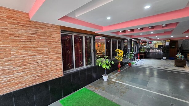 A hotel lobby with a modern design, featuring a reception desk, potted plants, and a green carpeted area. - Anandaloke Guest House (Kolkata)