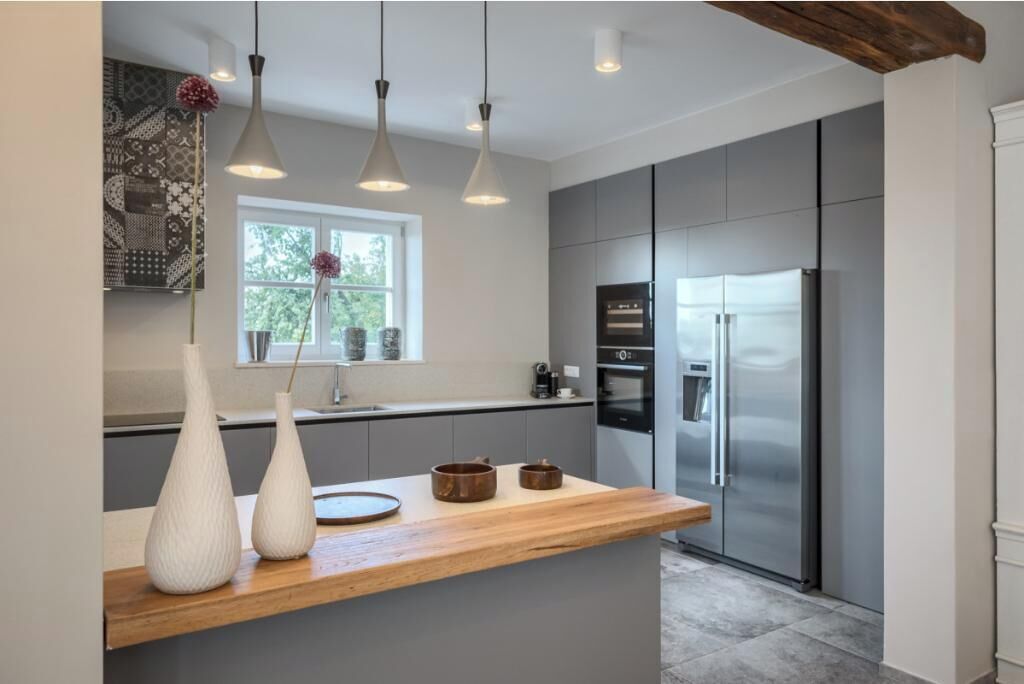 A modern kitchen with a wooden countertop, stainless steel appliances, pendant lighting, and a window with a view of greenery.