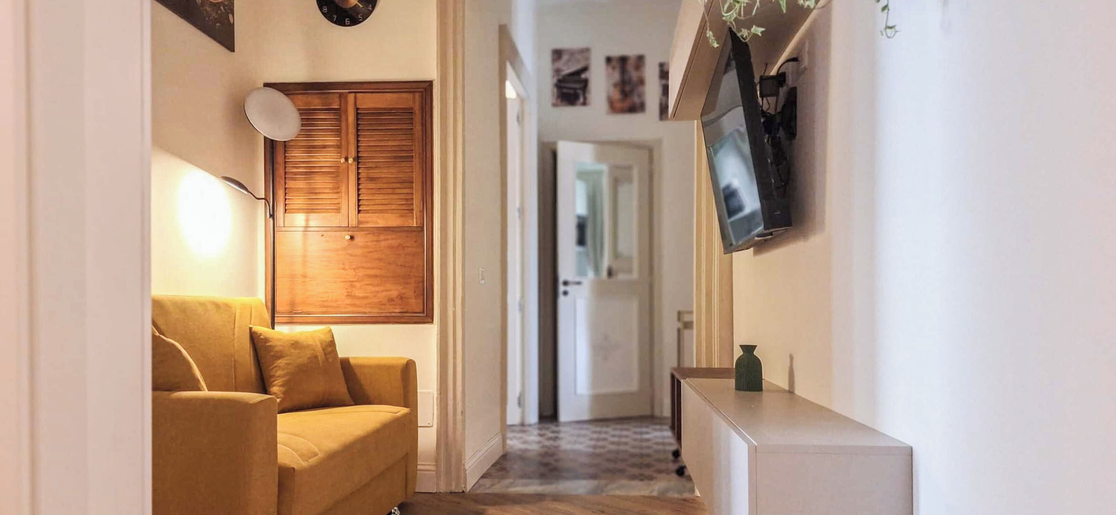 Un couloir avec un canapé, une porte en bois, un téléviseur fixé au mur et un petit meuble.