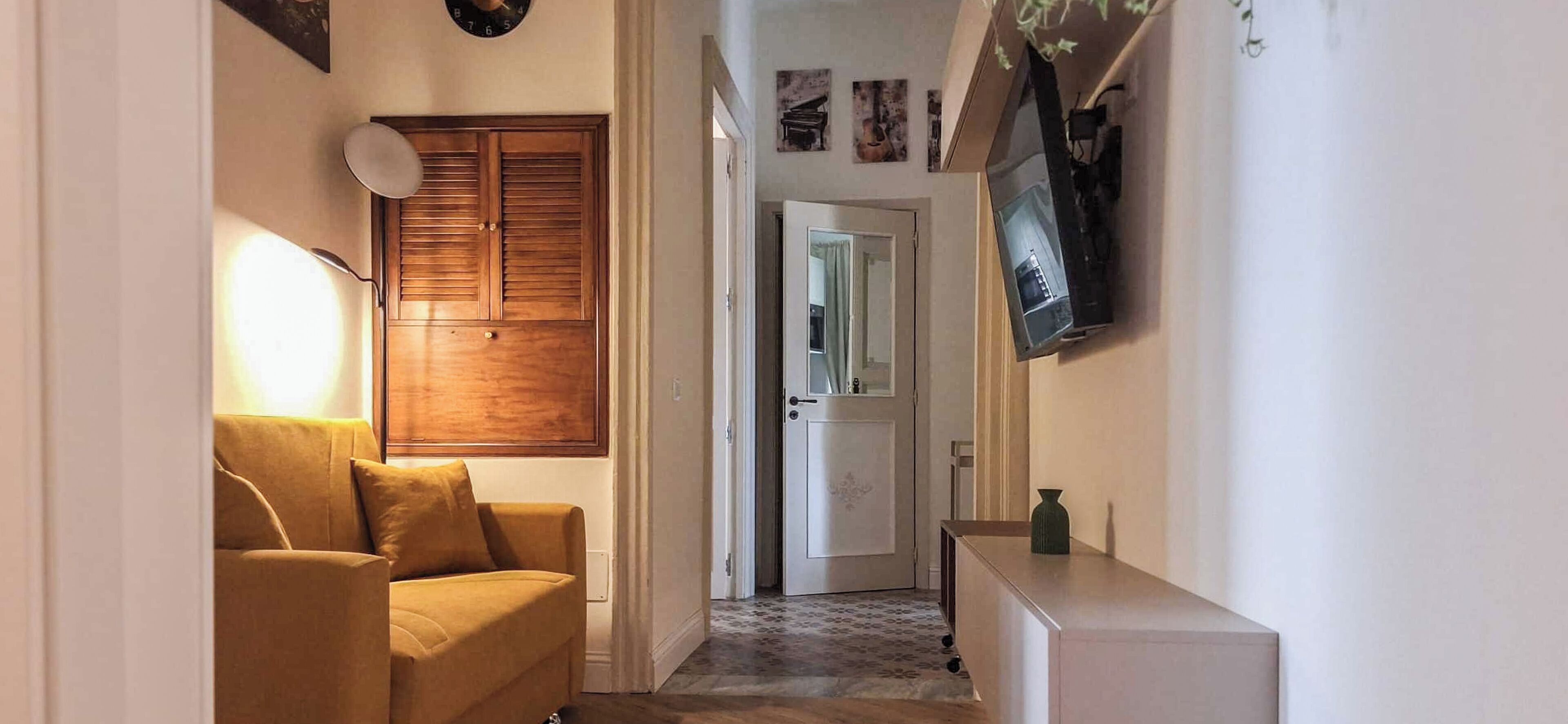 A hallway with a sofa, a wooden door, a TV, and a small cabinet.