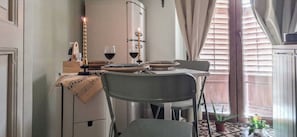Un comedor con una mesa dispuesta para dos, un refrigerador blanco y una ventana con persianas.