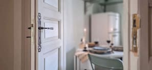 Una puerta blanca con picaporte metálico y cerradura, que da paso a una habitación con una mesa y sillas.
