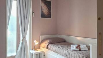 A bedroom with a bed, a bedside lamp, a window with curtains, and a wall-mounted picture.