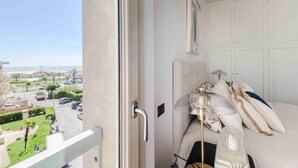 Ein Balkon mit Blick auf einen Parkplatz und Gebäude, ein Bett mit Kopfteil, ein Nachttisch und eine Lampe.
