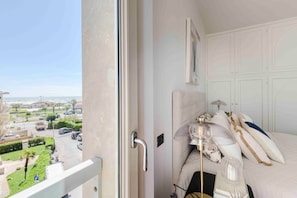 Ein Balkon mit Blick auf einen Parkplatz und Gebäude, ein Bett mit Kopfteil, ein Nachttisch und eine Lampe.