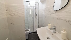 A bathroom with a glass-enclosed shower, a white sink, a mirror, and a toilet. - IL GIRAMONDO (Noto)