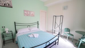 A room with a bed, a bedside table with a lamp, a chair, and a small table. - IL GIRAMONDO (Noto)