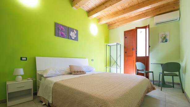 A bedroom with a bed, nightstand, and a green wall. - IL GIRAMONDO (Noto)