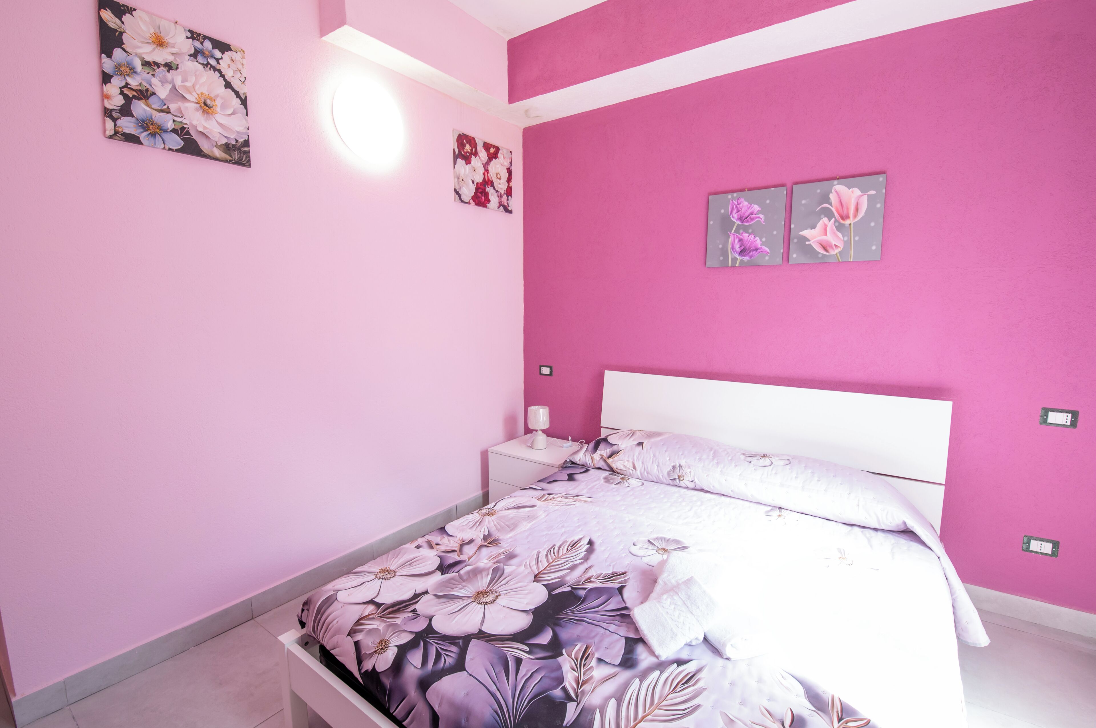 A pink-themed bedroom with a bed, nightstand, and wall art.