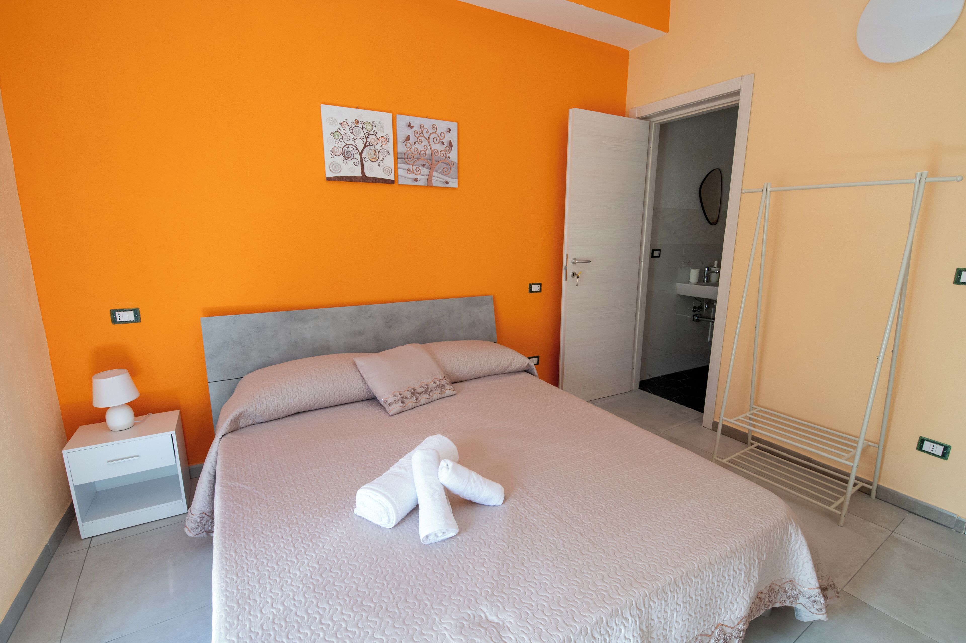 Un dormitorio con cama, una mesita de noche, un estante en la pared y una puerta que da al baño.