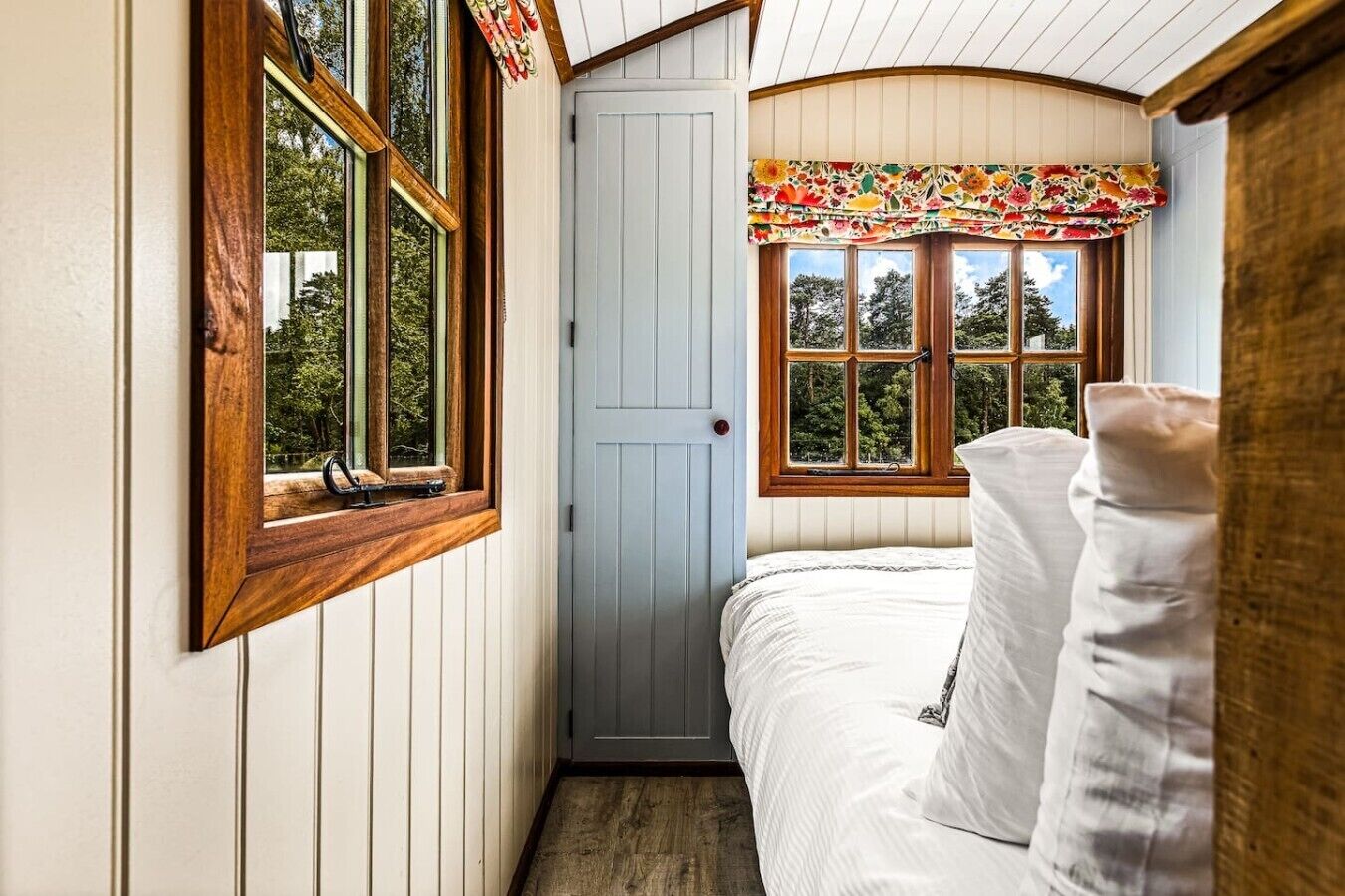 A narrow room with a bed, a door, and two windows with curtains.