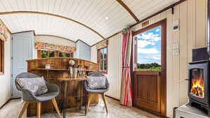 A cozy room with a curved ceiling, a wooden table with chairs, a fireplace, and a view of the outdoors. - Hamble Brook in Oakengrove Vineyard (Buckinghamshire)