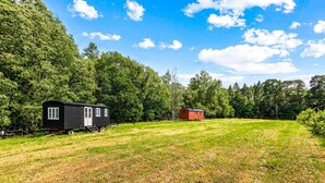 A black mobile home with a white door and windows, a red mobile home, and a grassy field with trees in the background. - Hamble Brook in Oakengrove Vineyard (Buckinghamshire)