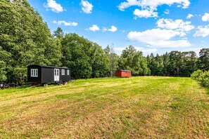 Une maison mobile noire avec une porte et des fenêtres blanches, une maison mobile rouge, et un champ verdoyant avec des arbres en arrière-plan.