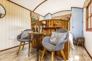 A cozy room with a curved ceiling, wooden furniture, a small table with a bottle and glasses, and a blue door.