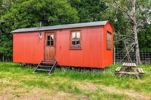 Une petite cabane en bois rouge, avec une porte, des fenêtres et un petit porche.