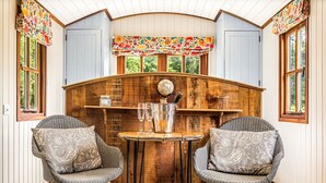 A cozy room with wooden walls, a round table, two wicker chairs, and a decorative clock. - Hamble Brook in Oakengrove Vineyard (Buckinghamshire)
