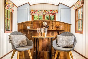 A cozy room with wooden walls, a round table, two wicker chairs, and a decorative clock.