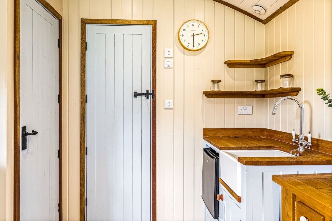 Une cuisine avec des meubles de rangement en bois, un évier, une horloge et une porte.