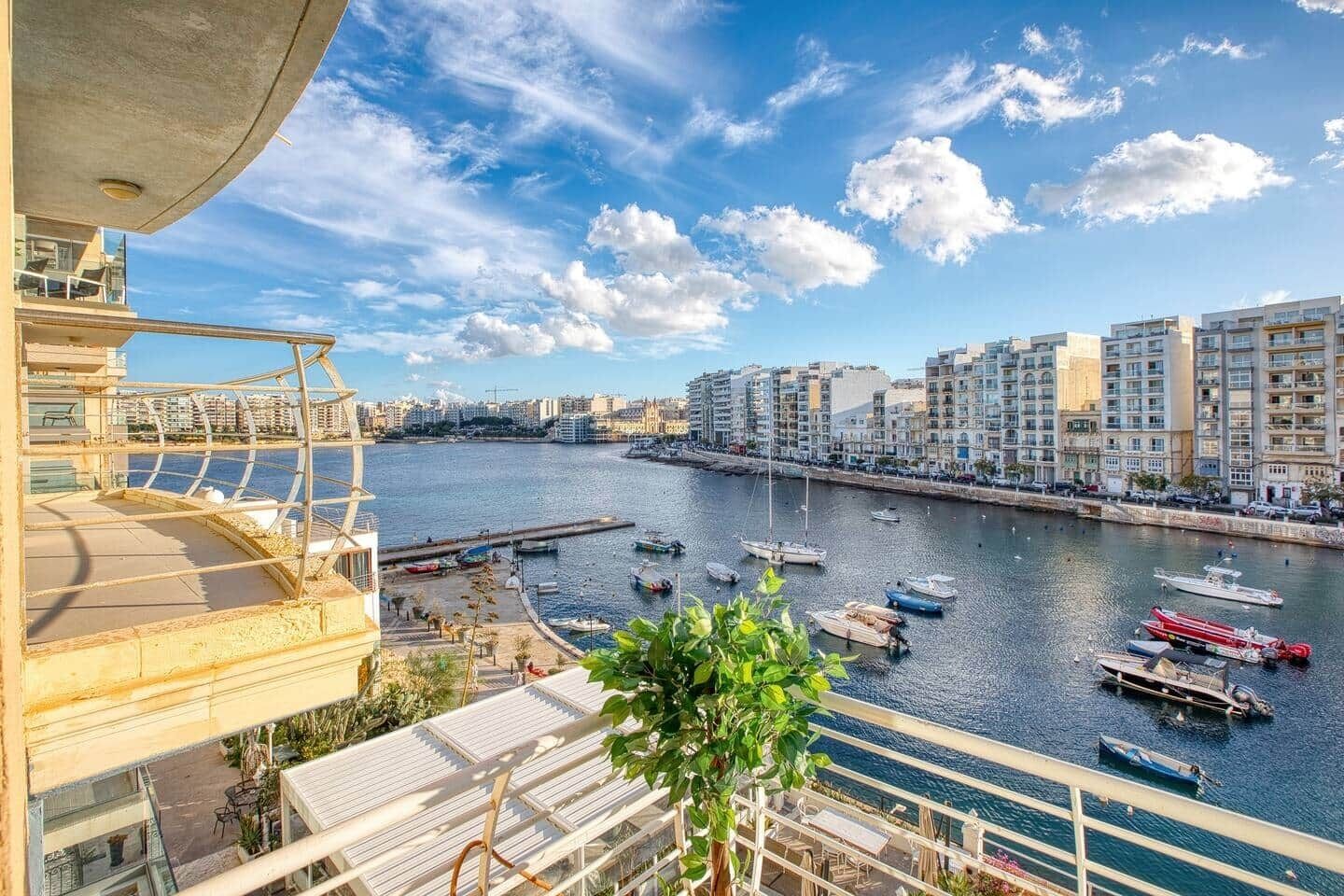 A waterfront view from a balcony with a marina, buildings, and a clear sky.