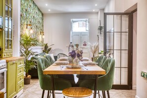A dining area with a wooden table set for four, green upholstered chairs, and a potted plant. - Casa Botanica, charming Maltese townhouse (Luqa)