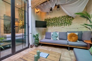 A modern room with a glass door, a sofa, a flat-screen TV, and a wall-mounted plant grid. - Casa Botanica, charming Maltese townhouse (Luqa)