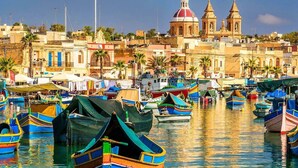Un puerto deportivo con numerosas embarcaciones coloridas amarradas, una iglesia destacada con cúpula roja, y un paisaje urbano costero al fondo.