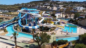 Un parque acuático con múltiples toboganes y piscinas, rodeado de palmeras y un paisaje montañoso.