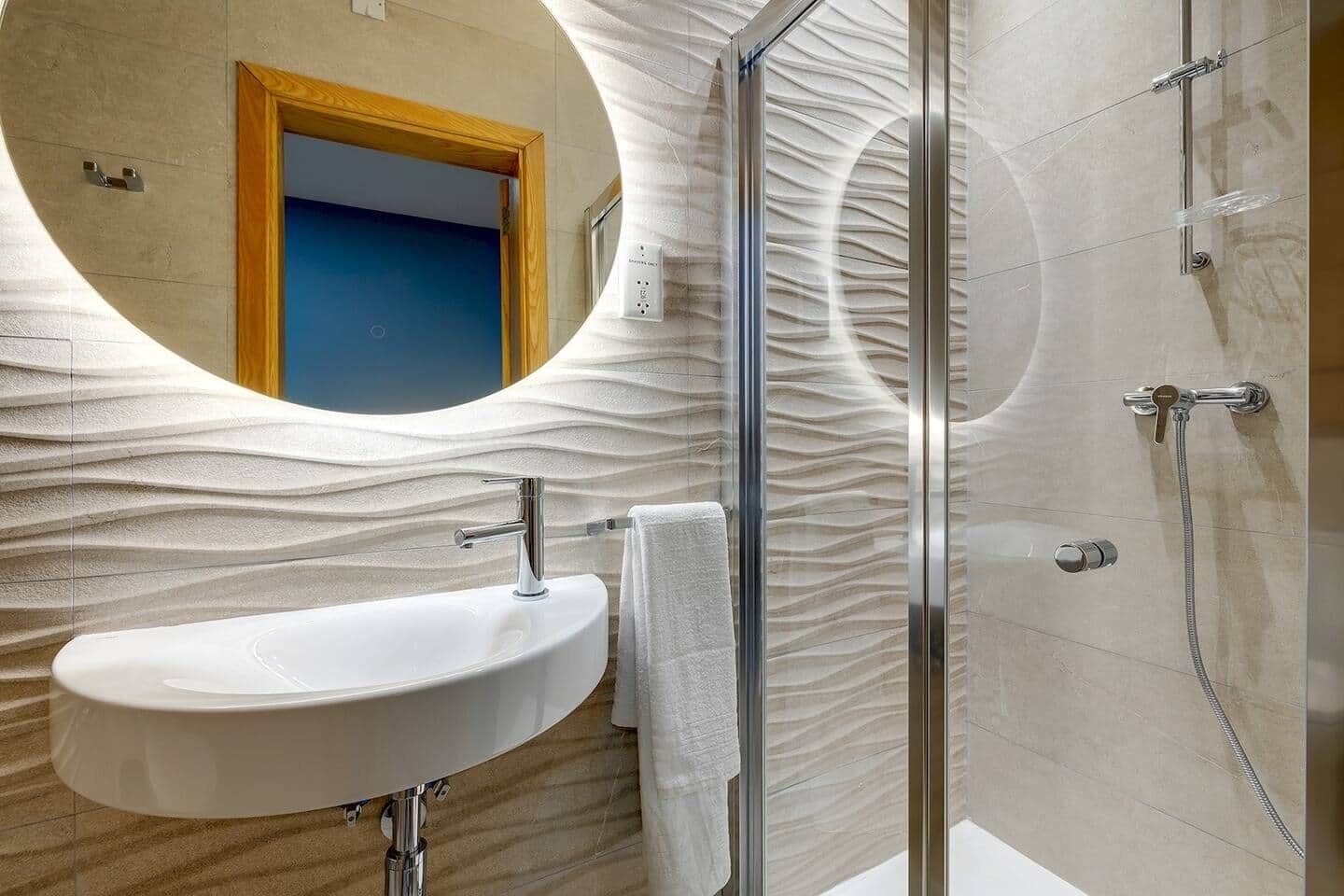 A bathroom with a white sink, a glass shower enclosure, and a mirror with a wavy design.
