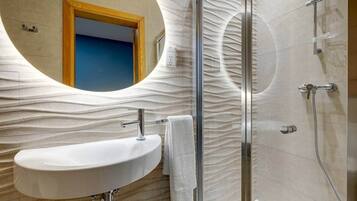 A bathroom with a white sink, a glass shower enclosure, and a mirror with a wavy design.