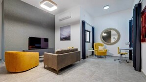 Una sala de estar moderna con un sofá, un sillón amarillo, un televisor y un espejo redondo.