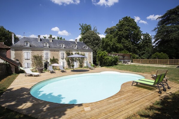 Une piscine avec une terrasse en bois, des chaises longues et une maison en arriĂšre-plan.
