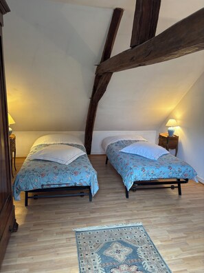A bedroom with two beds, wooden beams, a rug, and bedside lamps.