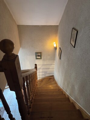 Un escalier en bois avec une rampe, un luminaire fixé au mur et des tableaux encadrés.