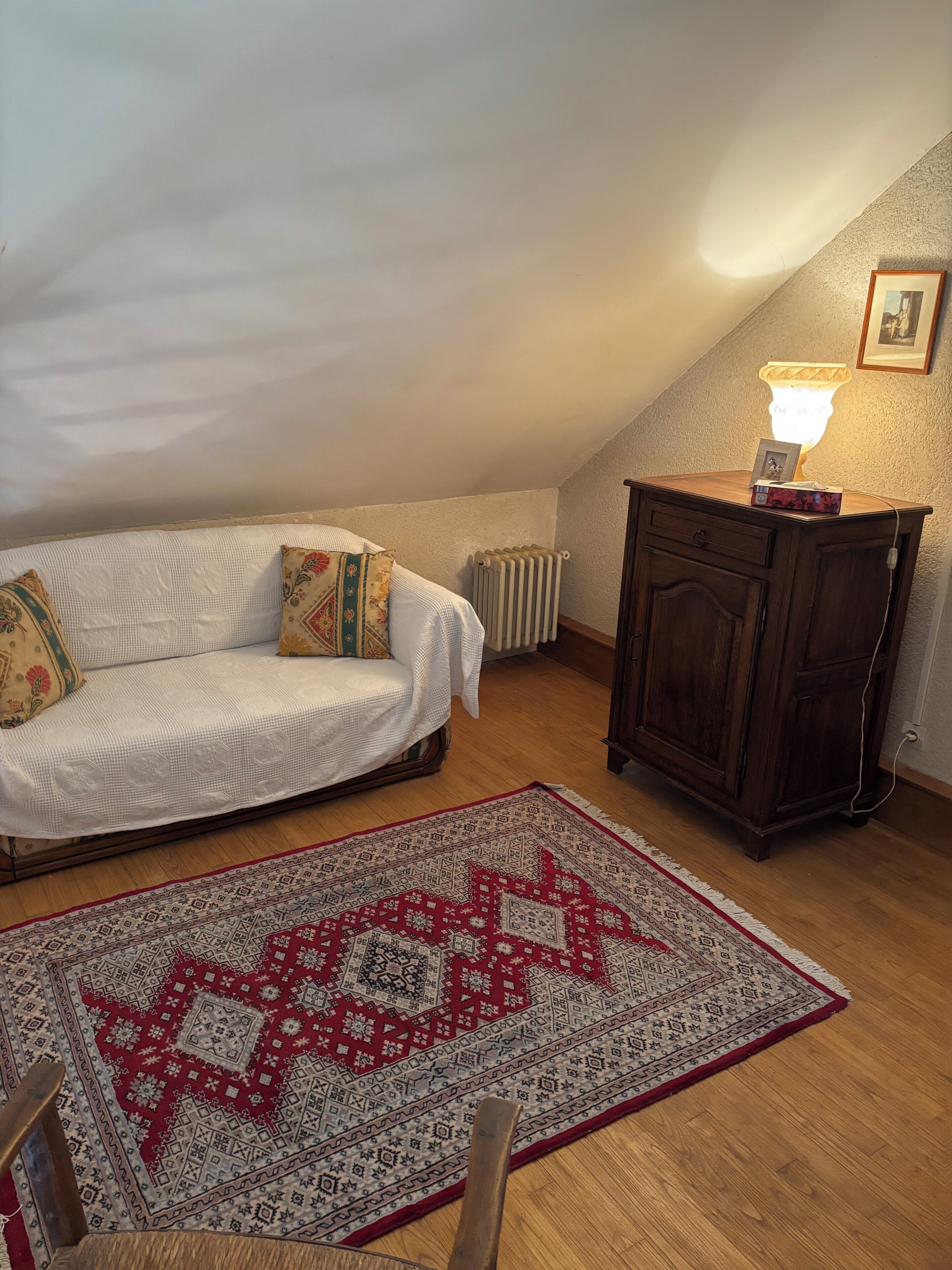 Um quarto acolhedor com um sofá branco, um tapete estampado, um armário de madeira e um radiador.