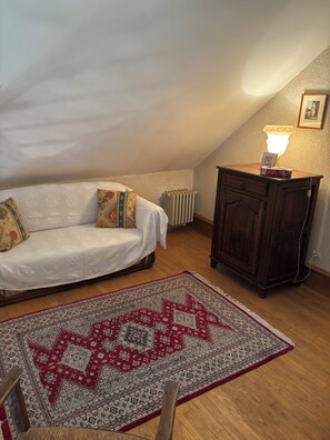 A cozy room with a white sofa, a patterned rug, a wooden cabinet, and a radiator.