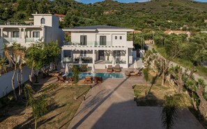 Eine moderne Villa mit Swimmingpool, Sitzgelegenheit im Freien und Blick auf die umliegenden Hügel.