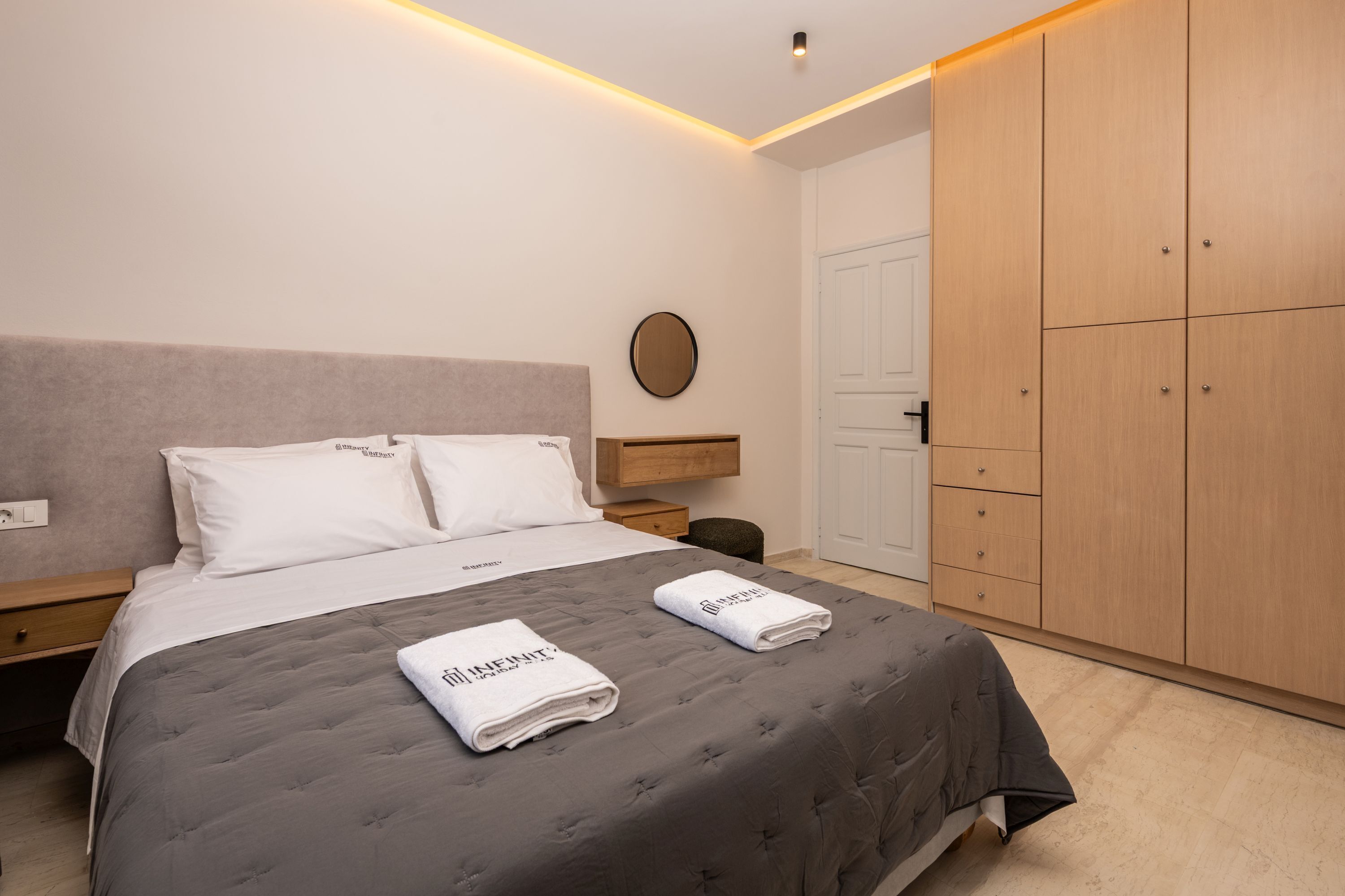 Un dormitorio moderno con una cama, mesitas de noche, un armario de madera y un espejo redondo en la pared.