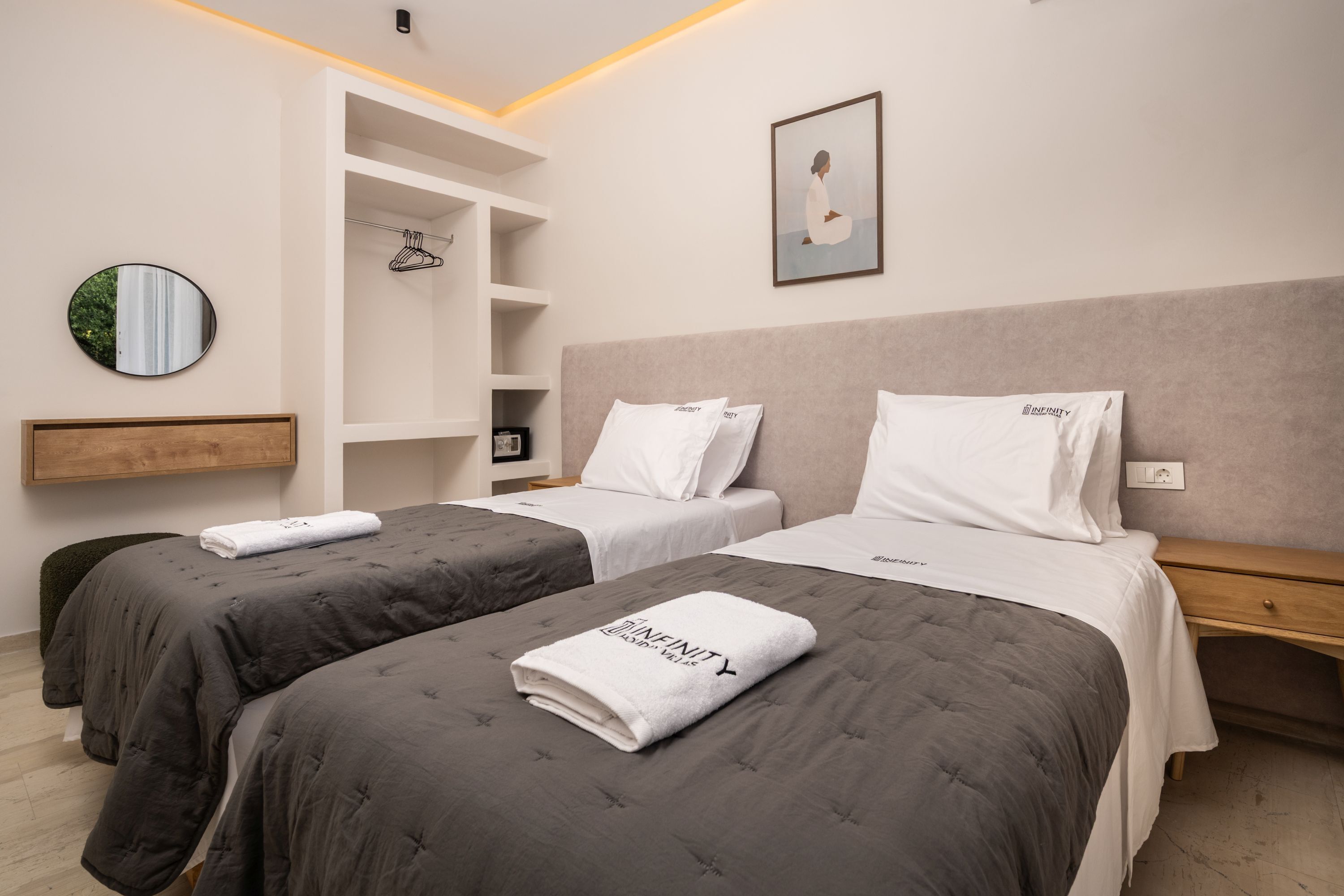 A hotel room with two beds, a wardrobe, a mirror, and a framed picture on the wall.