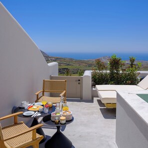 A terrace with a table set for breakfast, wicker chairs, a sofa, and a view of the sea. - Avelora Suites (Pyrgos Kallistis)
