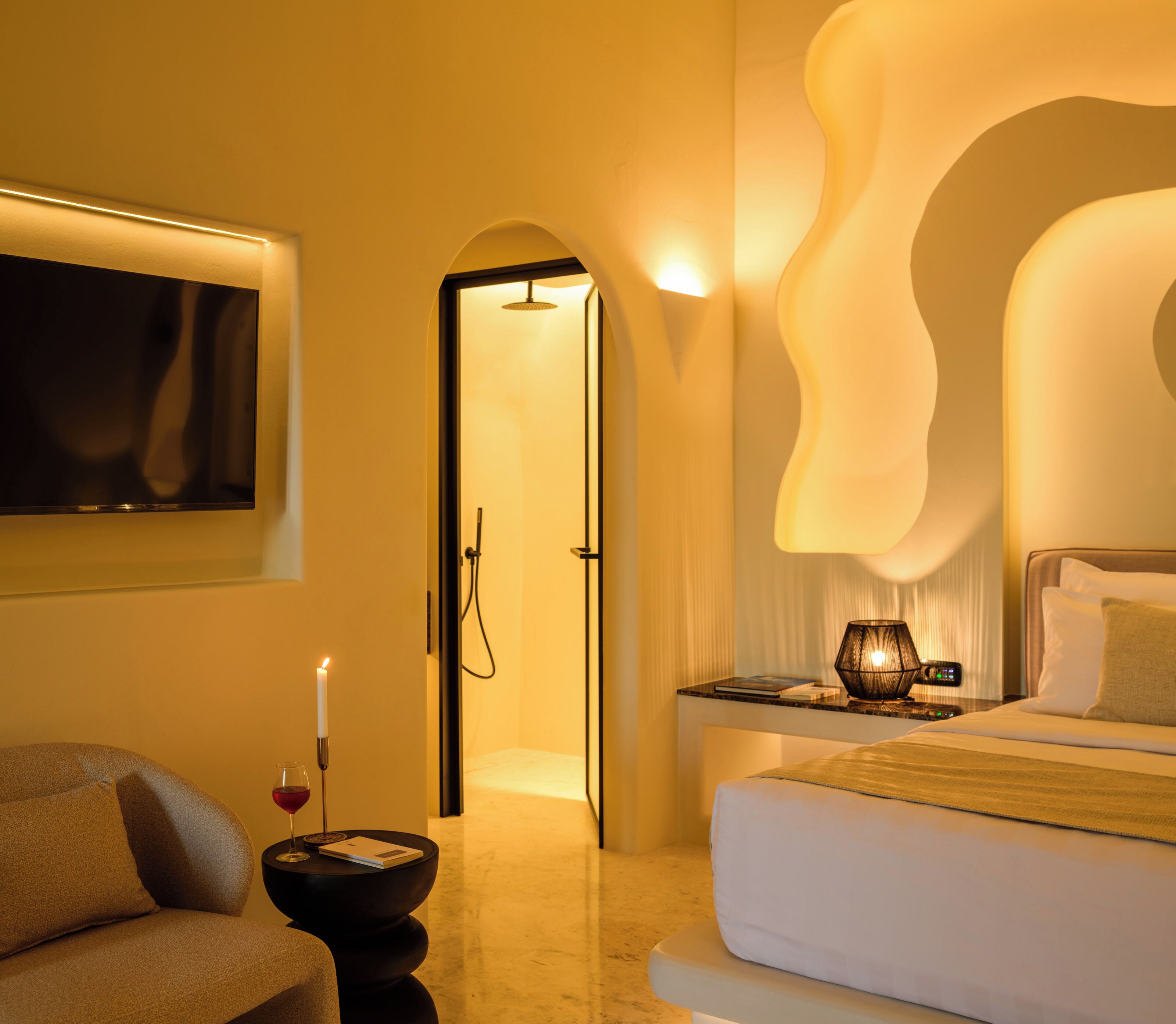 A hotel room with a bed, a nightstand, a lamp, a TV, and a door leading to a bathroom.