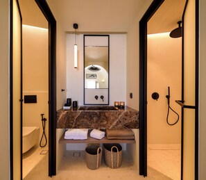 A modern bathroom with a marble sink, a large mirror, a towel rack, and a shower area. - Avelora Suites (Pyrgos Kallistis)