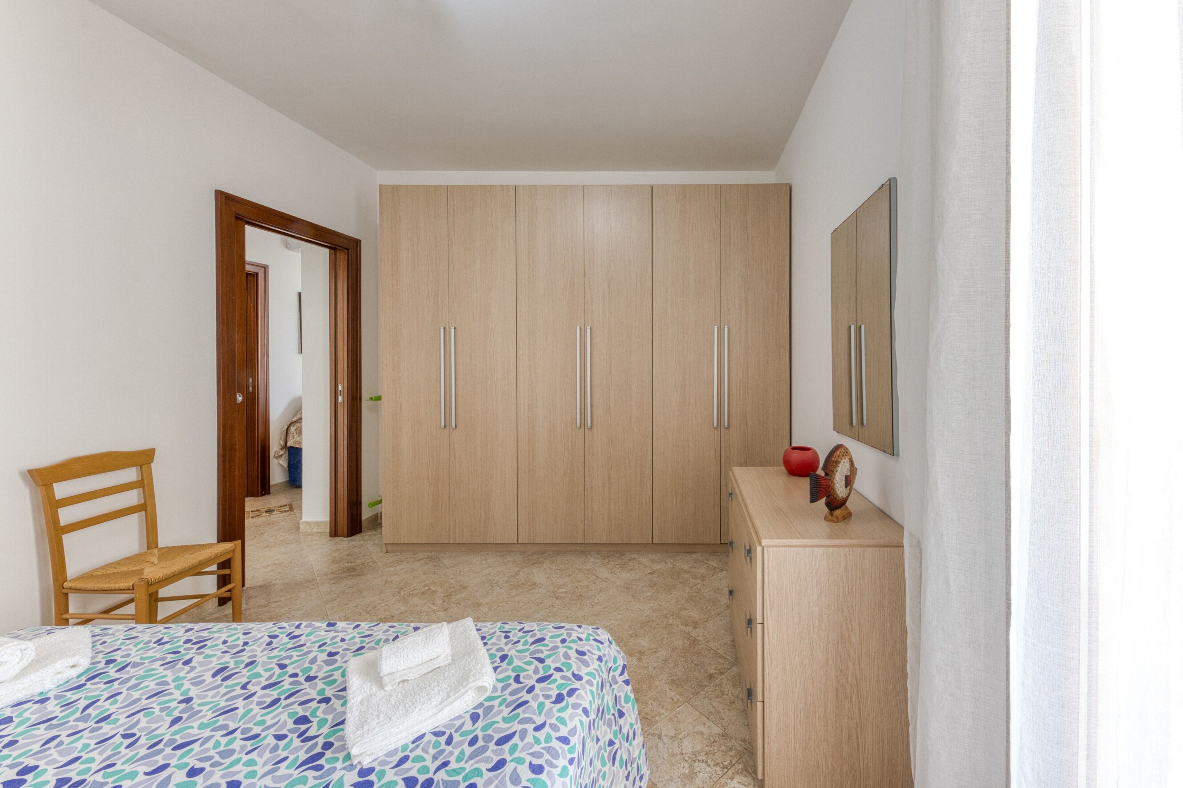Un dormitorio con cama, un armario de madera, una silla y un espejo en la pared.