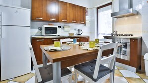 Eine moderne Küche mit Holzausbau, einem weißen Kühlschrank, einer Mikrowelle und einem Esstisch mit Stühlen.