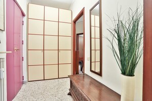 Un corridoio con una porta rosa, una panca in legno, uno specchio e una pianta in vaso.