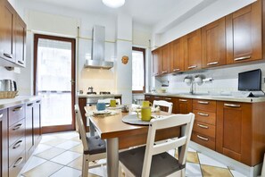 A modern kitchen with wooden cabinets, a dining table with chairs, and a large window. - GuestHost - Giuliana & Antonio in Montedonzelli (Napoli)