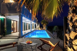Ein moderner Poolbereich mit einem klaren, blauen Pool, Liegestühlen und einem Tisch mit Früchten.