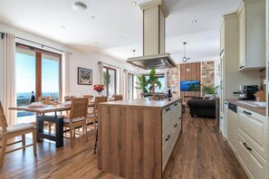 Eine moderne Küche mit Holzboden, einer zentralen Kochinsel und einem Essbereich mit Tageslicht.