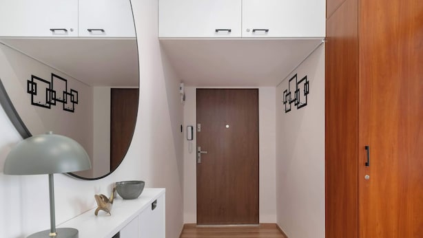 Un pasillo con una puerta de madera, una consola blanca con una lámpara y un cuenco decorativo.
